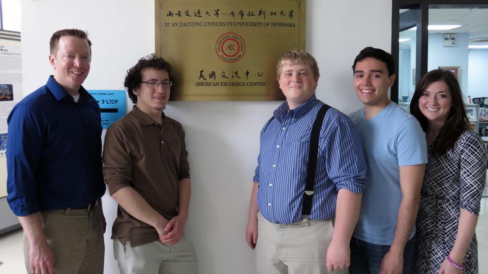 5 speech and debate team members standing in front of a golden plaque.